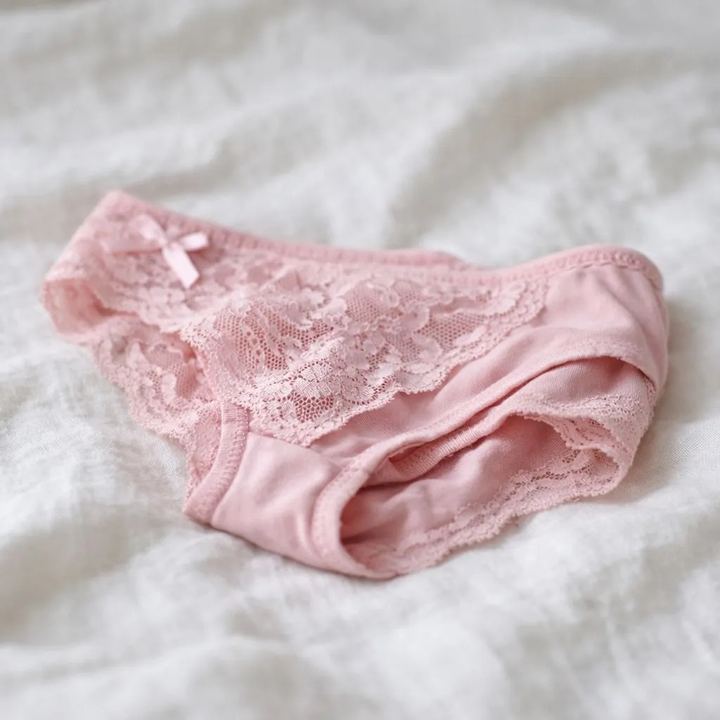 Culotte rose en dentelle portée, posée sur un lit
